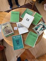 Top down image of multiple art magazines on a table with green and illustrated covers showing The Studio and Connoisseur issues.