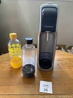 Front view of SodaStream sparkling water machine with two SodaStream bottles (grey and yellow) placed on wooden table.