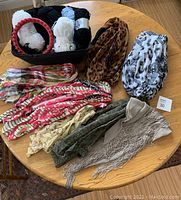 Various scarves including two infinity scarves and multiple other patterned scarves spread on a table beside the basket.
