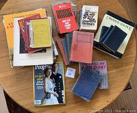 Various books laid out on a wooden table. Includes different genres such as Canadian history, fiction, crossword dictionaries, creative source books, and magazines.