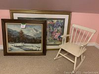 Photo showing all three items together: floral print in gold frame, wilderness painting in wood frame, and white child rocking chair.
