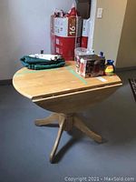 Wooden drop leaf table with paint splatter and wear on the surface, showing drop leaves down and a rounded end.