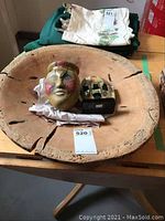 Top view of large wood turned bowl containing ceramic mask on stand and small ceramic face container