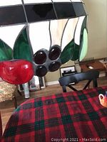 Close-up of stained glass panel showing red and purple fruit and green leaves on the fixture above a red plaid tablecloth.