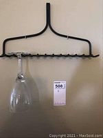 Front view of black metal rake head wine glass rack mounted on wall holding one upside-down wine glass hanging by the base from metal prongs.