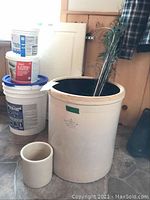 Large beige Imperial crock size 8, 18 inches tall, with smaller crock and peacock feathers inside, next to buckets.