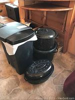 Photo of canning pot with jar holder, roaster, stew pot, and step-on waste container all grouped together on floor.