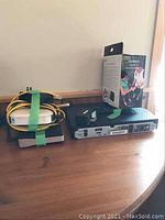 Photo of LG DVD player, D-Link VPN router, connected cables and Garmin eTrex 10 boxed device on wooden table.