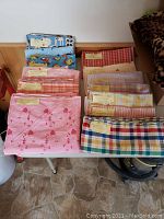 Photo showing an assortment of folded gingham, flannel, and plaid fabric pieces in various colors including red, blue, yellow, and mixed patterns on a table.