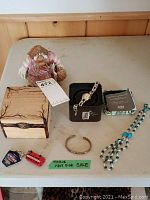 Full view of the lot items including the Fossil watch in box, wooden keepsake box, duck figurine, copper bracelet, beaded necklace, and keychains