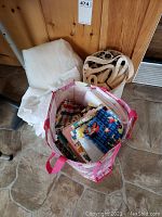 Photo shows pink reusable bag filled with multiple folded quilting fabric pieces in various colorful and patterned designs, white folded fabric or interfacing, and beige bag next to it.