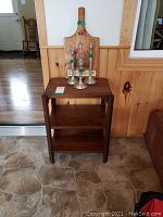 Front view of wood side table with three candlesticks and folk art cutting board on top