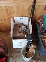 Box containing 8 brown curtain panels folded inside with a rod and hardware on top near a plastic storage bin.