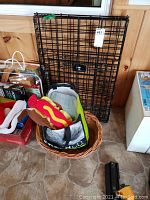 Photo showing folded black metal wire collapsible dog crate, wicker dog bed, and assorted dog bags including dog costume.