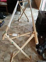 Full view of Mary Maxim quilt frame showing wooden structure, X-shaped cross braces, and cloth rods wrapped with fabric.