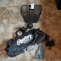 Metal mesh bicycle basket, Rawlings baseball bag, training wheels, and plastic bag with tent pegs on floor.