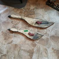 Two wooden painted geese in white and black with attached red hearts and wire hangers, placed on stone floor