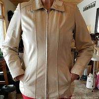 Front view of beige leather jacket showing zip front, collar, side pockets, and fitted seams