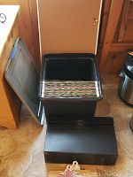 Black plastic file box with lid, showing hanging file folders inside and a portable accordion file inside.