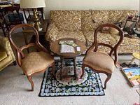 Two wood side chairs with upholstered seats, a wood drop leaf table with coasters and a doily on top, floral rug underneath, and surrounding living room furniture