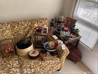 Overview of loveseat with assortment of decorative items including framed art, display case, bowl and container