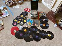 Symphonic record player with a collection of black and colored vinyl records arrayed on carpet.