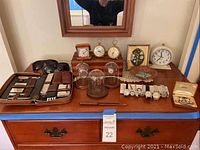 Overview of dresser top showing grooming kit, clocks, glass cloches, wood bowl, wood box, sunglasses, wristwatches, cufflink set