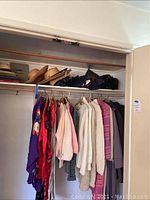 Overview of hanging vintage sweaters, coats, jackets, and Asian dresses on closet rod, with hats and handbags on upper shelf