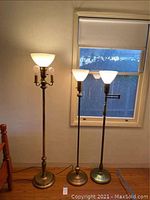 Full view of all three floor lamps, showing sizes and basic design: tallest lamp with triple lights and two shorter lamps with single light