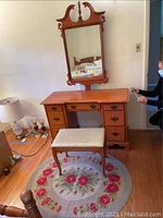 Front view of wood vanity dresser with attached mirror, bench on oval floral rug.