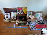 Overview of sewing machine, patterns, magazines, accessories and fabric remnants arranged in cases and boxes on floor
