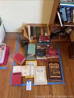 Overview of collection of vintage books, magazines and metal bookend arranged on the floor.