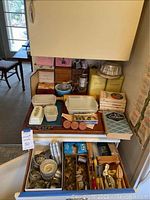 Wide angle of vintage bakeware assortment showing Pyrex dishes, cookbooks, recipe box, yellow cans for flour and sugar, metal sifter, rolling pin, jello molds, and kitchen utensils.