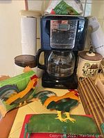 Photo showing Mr. Coffee drip coffee maker, rooster-themed napkin holder, and other rooster kitchen items.