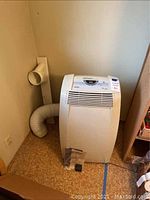 Front view of DeLonghi Pinguino PAC C100 portable air conditioner showing front grille and control panel with flexible exhaust hose attached to wall vent.