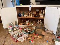 Wide shot of cabinet with shelf items and floor display including birdcage, banks, box of mini figurines and wood furniture