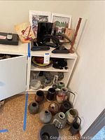 Overall view of white cabinet top and floor showing black candle holders, sculptural piece, wooden candlestick, art prints and floor vases