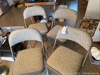 Four beige upholstered folding chairs with ribbed fabric seats and backs, metal frames.
