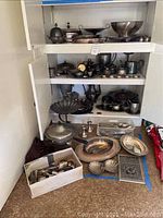 Overall shelf view with assorted silver plated pieces and flatware box at floor level