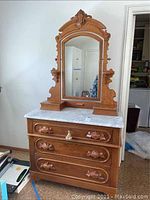 Full front view of the wood dresser with marble top and attached mirror showing carved details on the drawers and mirror frame.