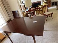 View of wood dining table with leaves in place and 2 chairs in background