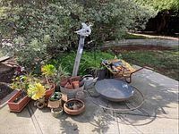 Showing the full collection of garden items including wheelbarrow, potted plants, fire pit, and gardening tools arranged outdoors on concrete.