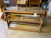 Angled side view showing entire wooden loom frame with some threaded yarn on rollers, placed on a garage floor near chairs and a fan.