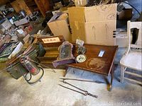 Wide view showing wooden coffee table with shelf, metal seed boxes to left, disassembled clock case and movement parts on table, fireplace tongs in front