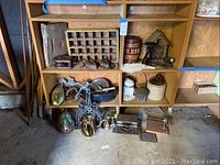 View of wooden multi-slot cubby organizer with various vintage and metal items placed inside and underneath, including a wooden barrel, flat irons, and carved wooden decoys.