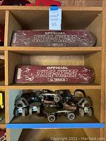Two red Official Skee-Skate by Tresco wooden skateboards on shelf above four pairs of roller skates
