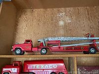 Wooden shelf view showing red ladder fire truck with extendable silver ladder and red hydraulic block