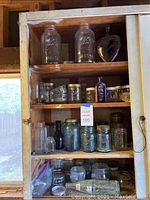 Full shelf view showing assorted glass jars and bottles of various sizes and types inside a wooden shelving unit.