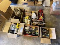 Overhead view of cardboard boxes filled with assorted tools and hardware items showing variety of hand tools, plumbing supplies and paint brushes.