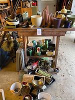 Front view of wooden potting bench loaded with assorted pots, planters, vases and bowls on the bench top, middle shelf and floor